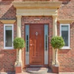 Golden Oak UPVC Door with door knocker and Obscure Glass panes on either side. White narrow UPVC windows on each side of house.