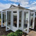 White UPVC Garden Room in the corner of garden with two sets White UPVC french doors, white upvc casement window with top opener and white UPVC fixed pane window